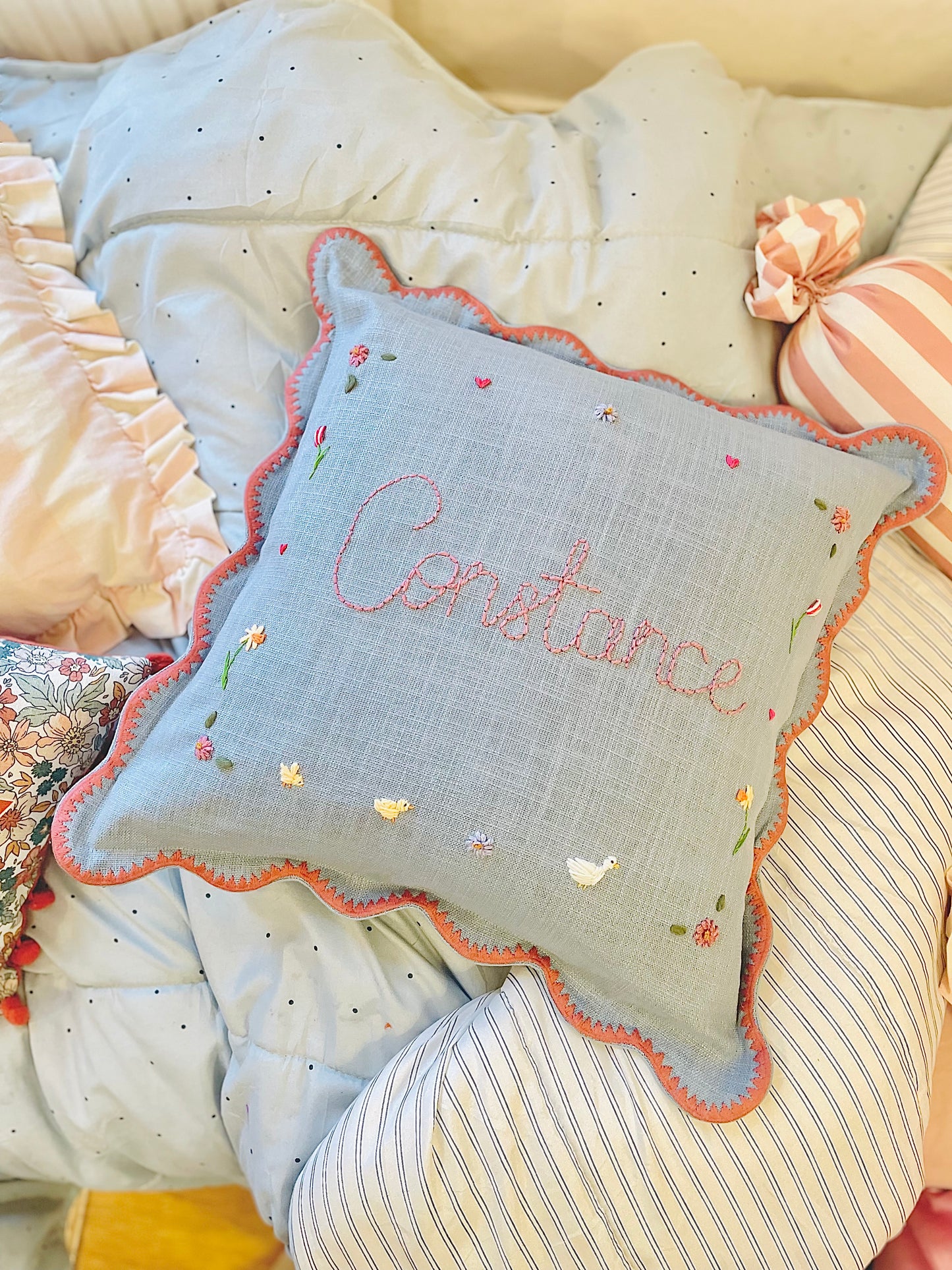 Decorative pillow with embroidered name on a bed with other pillows.